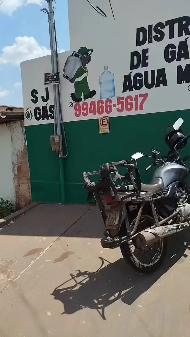 Fachada verde da SJ Gás com moto de entrega estacionada, foto real da loja em Anápolis.